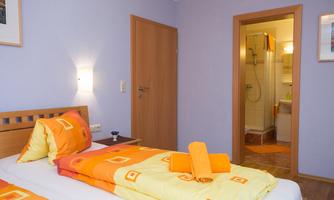 A bright room with two beds and colorful bedspreads. In the background, access to the bathroom is visible.