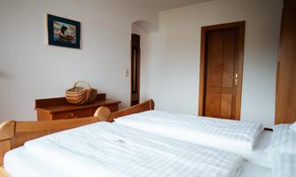 A cozy bedroom with two beds and white bedding. A picture hangs on the wall, and a wooden dresser is in the room.