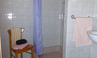 A bathroom with a shower, a chair, and towels. The walls are tiled and there is a small window with daylight.
