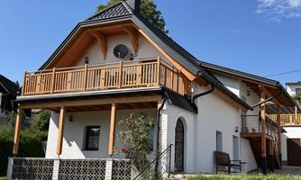 A modern house with a wooden porch and a beautiful garden. It has a bright facade and a clear blue sky in the background.