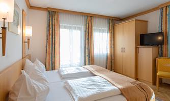 A cozy hotel room with two beds, a television, and a wardrobe. The windows are decorated with bright curtains, and the room feels inviting and harmonious.