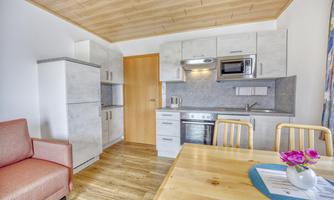 A modern kitchen with wooden ceilings and rustic furniture. The room includes a dining area and a seating corner.