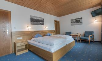 A cozy bedroom with a double bed and wooden paneling. There are two chairs and a table, as well as pictures on the walls.