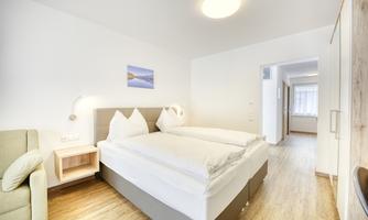 A modern bedroom with two beds and bright walls. The room is cozily furnished with an armchair and a small nightstand.