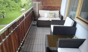 A cozy balcony with modern furniture and a tranquil view of greenery. The combination of wood and rattan creates an inviting atmosphere.