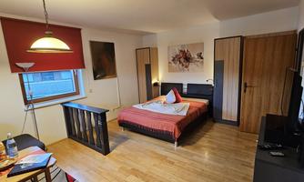 A cozy bedroom with a double bed and wooden furniture. There is a television, a table, and some decorative pictures on the walls.