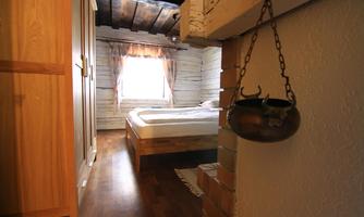 A rustic bedroom with a large bed and a window that lets in daylight. The room is furnished with wood and has a cozy character.