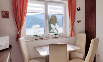 A bright dining room with a table and chairs. Through the window, there is a beautiful view of mountains and a lake.