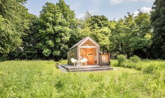 A small, modern house stands in the middle of a green meadow. Surrounded by trees, it offers a quiet and nature-friendly atmosphere.