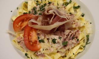 A plate of ribbon noodles, garnished with ham, tomato slices, and fresh herbs. The combination offers an appetizing and hearty meal.