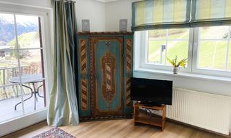 A cozy room with a colorful wardrobe and a television. Large windows offer a view of the green landscape outside.