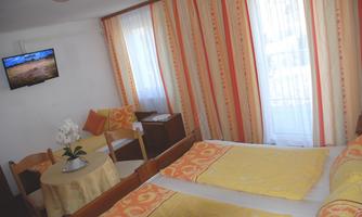 A cozy room with two beds, a table and chairs. Large windows let in plenty of daylight and there is a television on the wall.