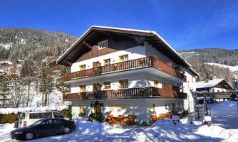 A cozy building in winter with a snow-covered ground. The surroundings are surrounded by mountains and trees.