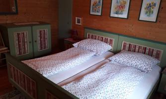 A cozy bedroom with a double bed and floral bedding. Pictures of flowers hang on the walls, and a wardrobe is in the room.