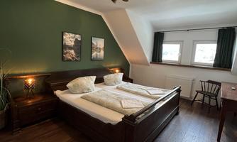 A cozy bedroom with a large double bed and wooden floor. The walls are painted green and there are windows with curtains.