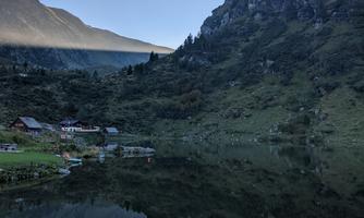 A tranquil mountain lake with mirrored water and surrounding green hills. In the background, majestic mountains can be seen.