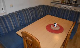 A cozy dining area with a blue couch and a wood and steel table. On the table, there is a round placemat with a decorative candle.