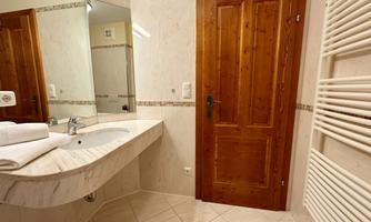 A modern bathroom with a sink and a large mirror. The walls are decorated with light tiles and wooden details.