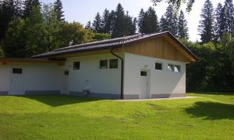 A modern building in a green environment, surrounded by trees. The clear sky and the meadow contribute to the tranquil atmosphere.