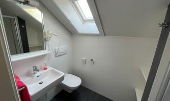 A modern bathroom with a sink, toilet, and a skylight. It has a bright, simple design and is well-lit.
