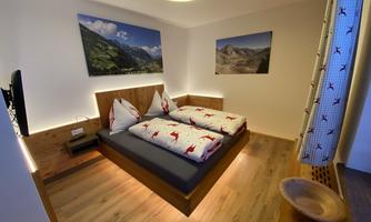 A modern bedroom with a double bed and cozy bedding. Pictures of landscapes hang on the walls and the room is well-lit.