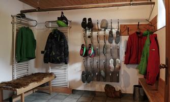 A spacious changing room with jackets and shoes. Rugs are lying on a bench and the floor is tiled.