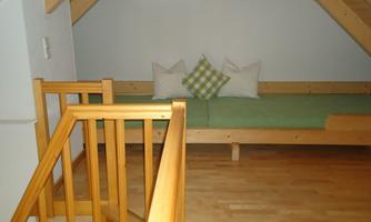 A cozy room in the attic with wooden paneling and a green lounge chair. On the lounge chair are two cushions, one of which has a checkered pattern.