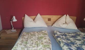 A cozy bedroom with a double bed and colorful blankets. The walls are red and there are pictures decorating the room.