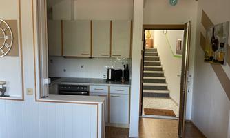 A functional kitchen with modern furniture and access to a staircase. The space is bright and inviting.