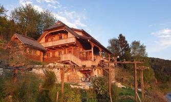 A cozy wooden house in a picturesque landscape. The evening sky is slightly orange and the moon is visible.