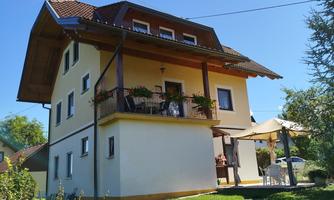A beautiful house with two floors and a balcony. The garden is green and sunny.