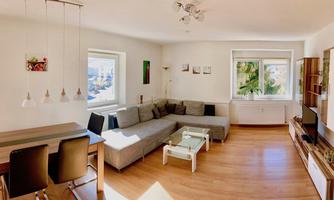 A modern living room with a large, bright sofa and a table. There are large windows that let in plenty of daylight.