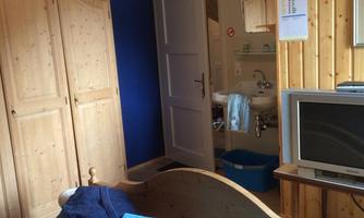 A cozy bedroom with a wooden bed and blue towels. In the background, a television and access to a bathroom are visible.