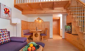 A cozy living space with wooden paneling and a staircase. There is a dining table, a couch, and fresh fruit on a table.