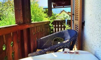 A cozy balcony with a table and a chair. In the background, there are trees and a clear sky.