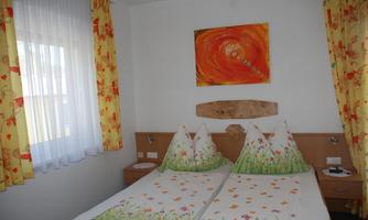 A cozy bedroom with two beds and colorful curtains. A colorful painting hangs on the wall.