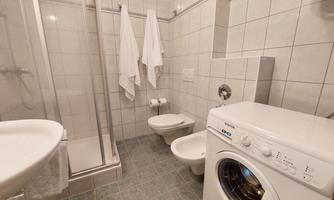 A modern bathroom with gray tiles. There is a shower, a toilet, and a washing machine.