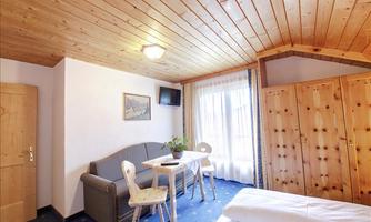A cozy room with a wooden ceiling and blue carpet. There is a table, chairs, and a view of a window with curtains.