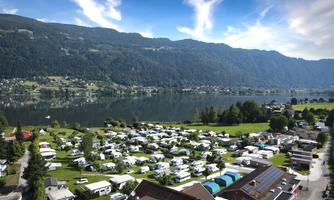 A quiet campsite by the shore of a lake, surrounded by green mountains. The sky is clear and blue, perfect for a relaxing stay in nature.