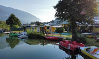 A peaceful waterway with colorful boats and a yellow house on the shore. In the background, mountains and trees are visible.