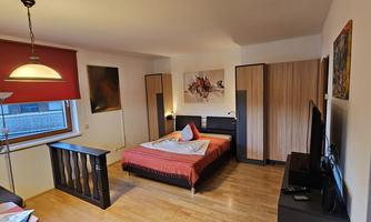 A cozy bedroom with a large bed and modern design. There is a television and a desk area, as well as some creative wall art.