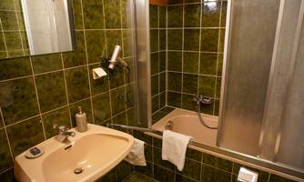 A bathroom with green tiles, a sink, and a shower cabin. The amenities include a hairdryer and towels.