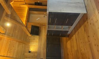 A cozy room with wooden walls and a wooden floor. There is a modern kitchen unit and a wall with a TV.