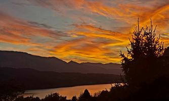 A breathtaking sunset over a tranquil lake, surrounded by mountains. The sky glows in warm shades of orange and yellow.