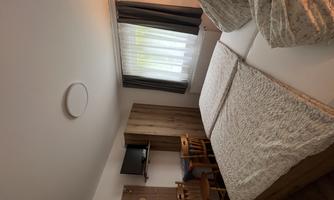 A cozy room with a double bed, table, and chairs. Large windows provide plenty of daylight.