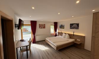 A modern bedroom with a large bed and light wood decor. The rooms are warmly furnished and have a table as well as a television.