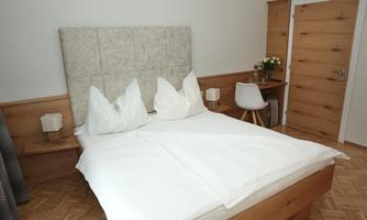 A cozy bedroom with a double bed and soft pillows. Next to the bed is a small table and a chair.
