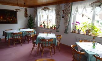 A cozy room with wooden tables and chairs. The windows are decorated with curtains, and small vases with flowers are on the tables.
