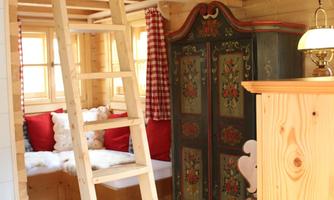 A cozy interior with wooden paneling, a ladder, and a sleeping area on the upper floor. The decor is rustic, with red accents and a beautiful wardrobe.