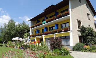 A charming residential building with colorful flower boxes and sunny balconies. The garden is well-maintained and the surroundings are green and inviting.